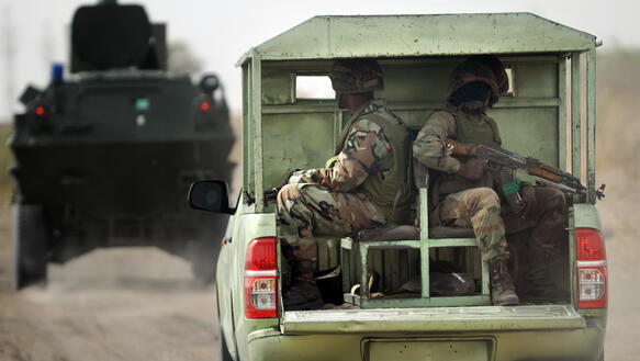 Zwei uniformierte Soldaten mit Gewehren sitzen auf der Ladefläche eines Jeeps.