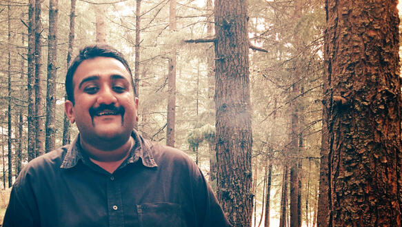 Ein mittelalter Mann, es ist der indische Amnesty-Mitarbeiter Abhirr-Velandy-Palat, steht in einem Nadelwald und lächelt.