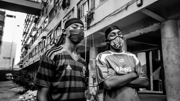 Zwei junge Männer in Fußballtrikots und mit Mundnasenschutzmasken, es sind die Brasilianer Kauan Alves und Alexandre Silva, stehen vor einem Wohnblock.