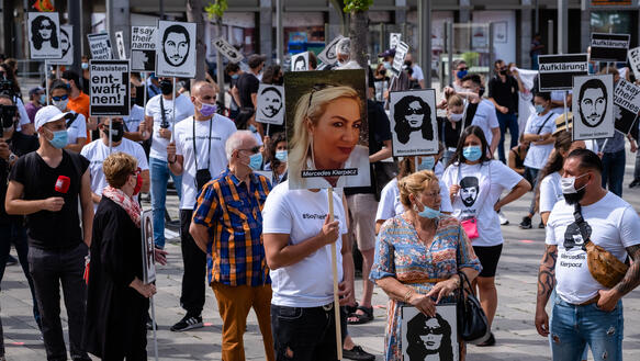 Menschen mit schwarz-weißen T-Shirts halten Schilder mit den Porträts der Ermordeten in den Händen