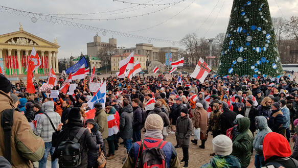Viele Menschen stehen auf einem großen Platz, sie tragen Jacken und Mützen, halten belarussische Flaggen in der Hand, auch eine EU-Flagge ist zu sehen