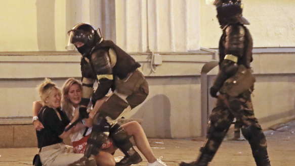 Zwei Polizisten in Kampfmontur nehmen zwei Frauen fest, die auf dem Boden sitzen, sie weinen, sind verängstigt