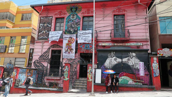 Ein Haus mit Transparenten und Plakaten in La Paz. Davor stehen zwei Frauen mit Sonnenschirmen.