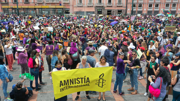 Eine Menschenmenge auf einem Platz, in der Mitte wird ein gelbes Spruchband hoch gehalten, auf dem "Amnistia" steht.