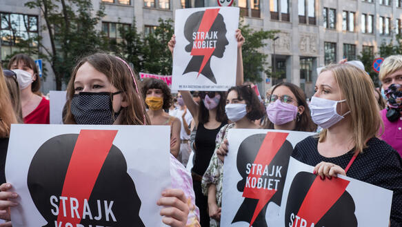 Mehrere Frauen mit Mundschutz halten Plakate hoch
