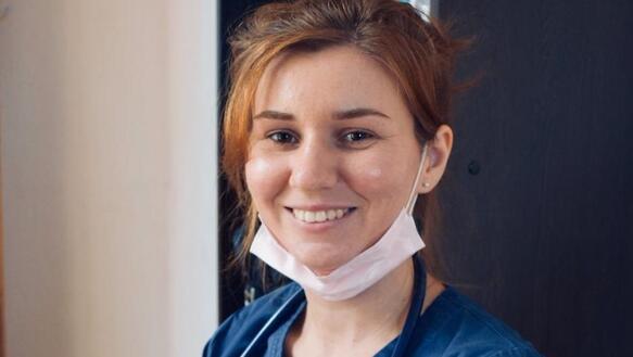 Eine junge Frau mit Stethoskop und Mundschutz um den Hals lacht freundlich in die Kamera.