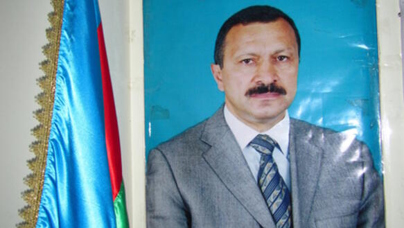 Ein Plakat eines Mannes mit dunklen Haaren und Schnauz in einem grauen Anzug, daneben ist die aserbaidschanische Flagge aufgehängt.