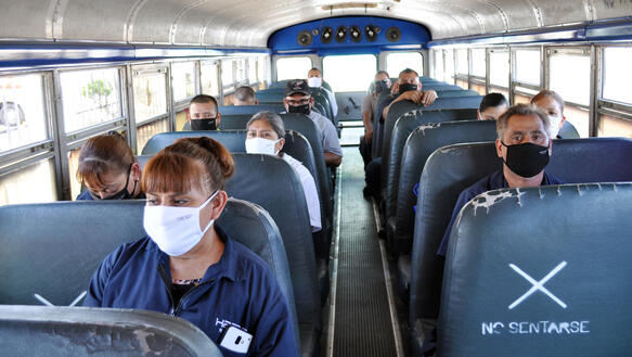 Menschen sitzen in einem Bus und tragen Mundnasenschutzmasken.