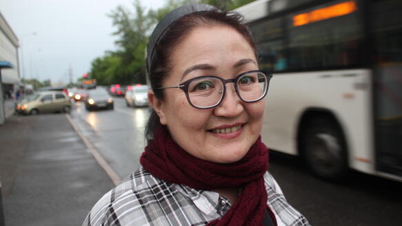 Portrait einer Frau, die in die Kamera lächelt. Sie ist auf der Straße, im Hintergrund ist ein Bus zu sehen.