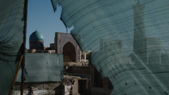 Blick auf eine Moschee, davor sieht man die Überreste eines Gebäudes. Ein grüner Sichtschutz grenzt die Baustelle ab