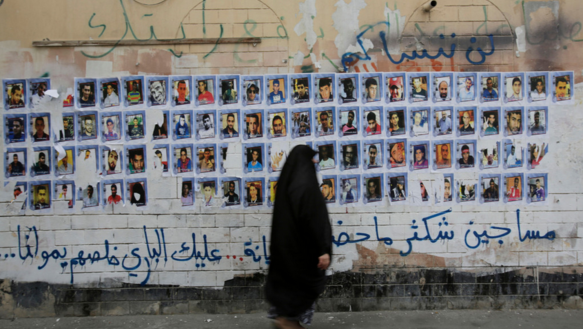 Eine Frau geht an einer Wand vorbei, an die zahlreiche Porträtfotografien geklebt