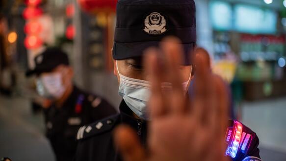 Das Bild zeigt einen Polizist mit Gesichtsmaske, die ihre Hand abwehrend vor die Kameralinse hält.