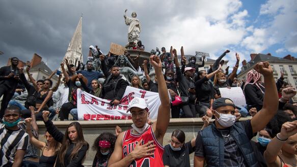 Das Bild zeigt eine Menschenmenge, in der Protestierende ihre Fäuste in die Luft halten.