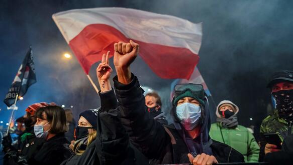 Nächtliche Frontalaufnahme von Protestierenden mit Maske und der polnischen Nationalflagge