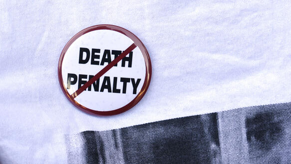 Das Bild zeigt einen Button (an einem T-Shirt) mit der Aufschrift "Death Penalty", die durchgestrichen ist.