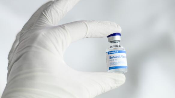 Das Bild zeigt einen Hand in einem Handschuh, mit einer Impf-Ampulle