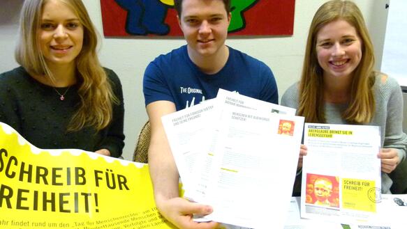 Zwei Schülerinnen und ein Schüler halten lächelnd unterschriebene Petitionen in die Kamera