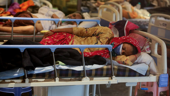 Das Bild zeigt  mehrere Krankenhausbetten, dicht nebeneinander, darauf liegen Menschen mit Schutzmasken