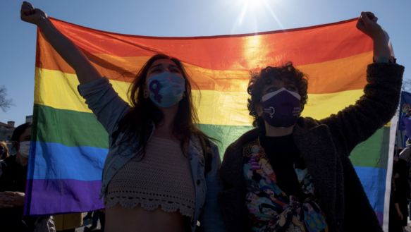 Das Bild zeigt zwei Personen, die eine Regenbogenflagge in die Höhe halten
