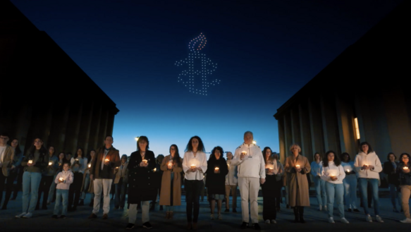 Das Bild zeigt viele Menschen mit Kerzen in der Hand, es ist Nacht, am Himmel sind Lichtpunkte zu sehen, die die Amnesty-Kerze symbolisieren