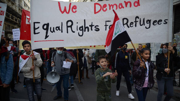 Demonstration von Kindern und Erwachsenen mit einem Banner mit dem Aufdruck "We demand equal rights for refugees".