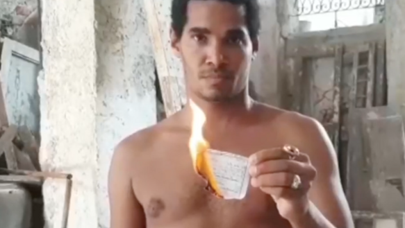 Ein junger Mann, oberkörperfrei, hält einem brennenden Zettel in die Kamera.