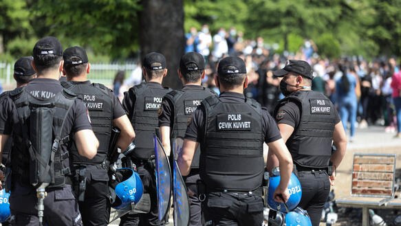 Polizisten im Vordergrund, sie tragen Mützen und schauen in Richtung einer Menschenmenge