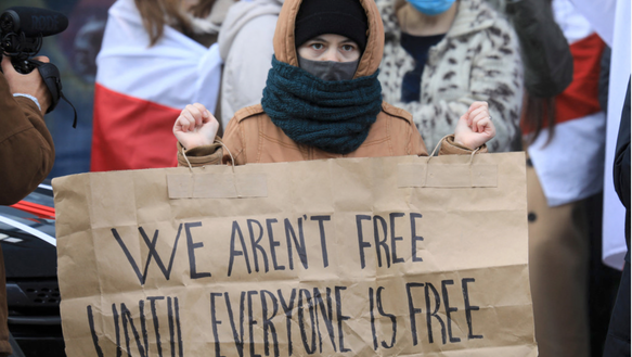 Das Bild zeigt eine junge Frau auf einer Demonstration mit dem Schild "We arent free until everyone is free"