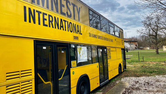 Das Bild zeigt einen gelben Doppeldecker-Bus mit Amnesty-Aufschrift