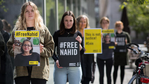 Fünf Frauen stehen versetzt hintereinander auf einem Fußfängerweg. Sie halten Schilder in die Kamera, auf denen unter anderem steht "Free Nahid" oder "This is not justice! #Evin".