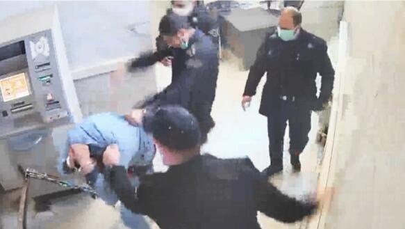 Das Foto zeigt die Aufnahme einer Überwachungskamera, die filmt, wie vier Männer in Uniform auf einem Flur um einen Mann in Gefangenenkleidung stehen. Zwei der Männer schlagen und treten auf den Gefangenen ein, der sich schützen die Hände hinter den Kopf hält.