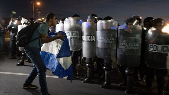 Ein Protestierender mit der Flagge Nicaraguas in der Hand steht vor Protest-Polizei und schreit in deren Richtung