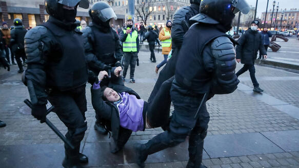 Das Bild zeigt Polizisten in schwerer Ausrüstung, wie sie eine Personen an Händen und Füßen davontragen.