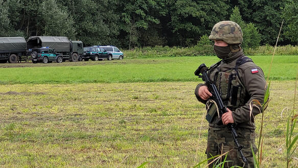 Das Bild zeigt einen Soldat mit schwerer Bewaffnung, er steht auf einem Feld, im Hintergrund ein Waldstück