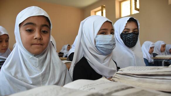 Das Bild zeigt drei Mädchen mit Kopftuch, sie sitzen in an einer Schulbank und lesen