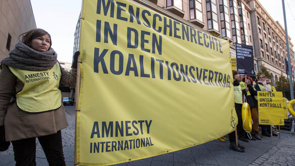 Das Bild zeigt mehre Personen mit Plakaten und einem Banner in gelber Farbe