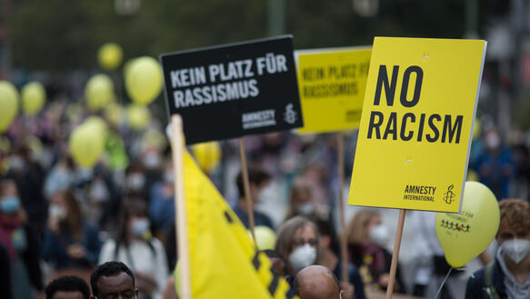 Eine Menschenmenge, auf einem Plakat steht: „No racism“.