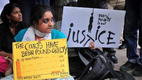 Das Bild zeigt eine Frau mit einem Schild "The courts have been found guilty" und "Death Penalty is not justice"