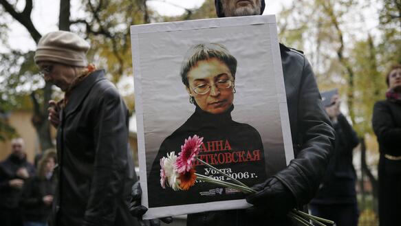 Das Bild zeigt eine Demonstration, im Vordergrund einen Mann mit einem Foto von Anna Politkowskaja und Blumen