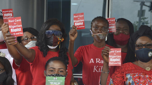 Das Bild zeigt mehrere Personen mit Protestkarten in der Hand "Red Card to Nigerian Rapists"