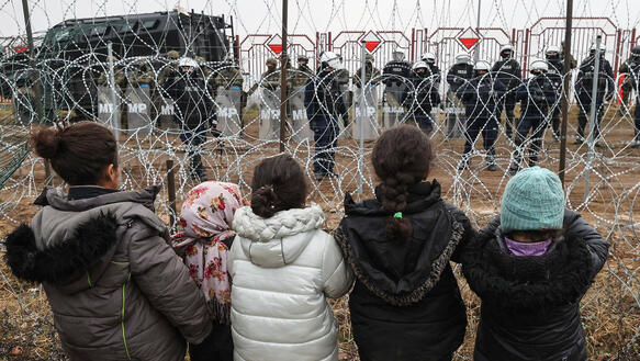 Das Bild zeigt Kinder, die an einem Zaun mit Stacheldraht stehen