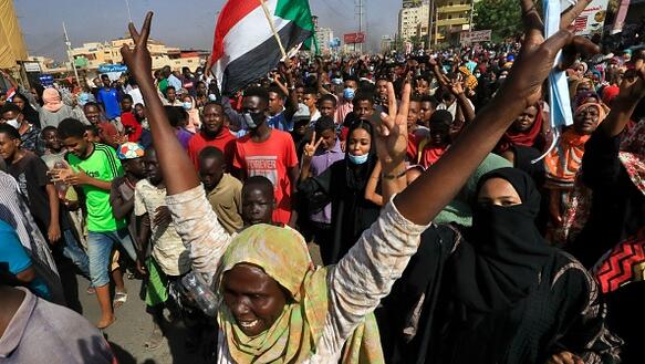 Das Bild zeigt eine Demonstration, viele Menschen und eine sudanesische Flagge