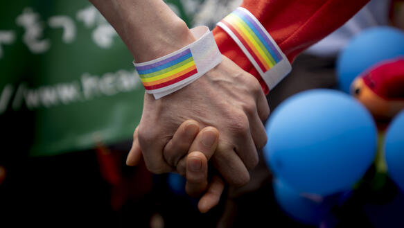 Das Bild zeigt zwei Hände mit Regenbogen-Armband
