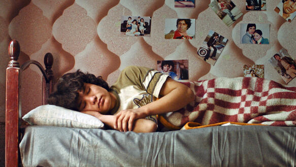 Ein Junge liegt auf der Seite in einem Bett und schläft, an der Wand hinter ihm hängen Fotos.