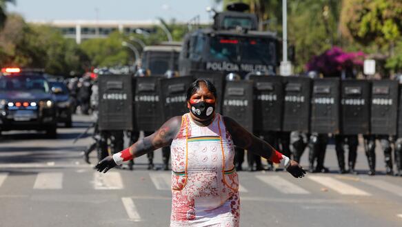 Eine Frau mit Gesichtsmaske steht in der Mitte einer Straße. Im Hintergrund ist Polizei.