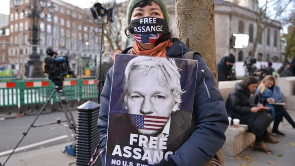 Das Bild zeigt eine Frau, die bei einer Demonstration ein Bild von Julian Assange hält und der Forderung "Free Assange"