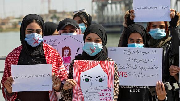 Das Foto zeigt eine Gruppe von sieben Frauen, die Kopftücher und Mundschutz tragen und Schilder mit arabischer Schrift und Zeichnungen vor sich halten.