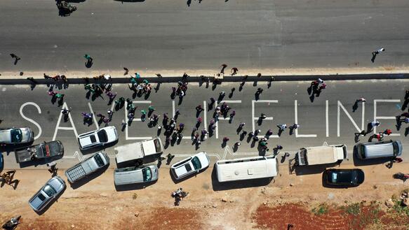 Drohnenfotografie einer Straße auf der sich Autos, viele Menschen und der Schriftzug "Save Lifeline" befinden.