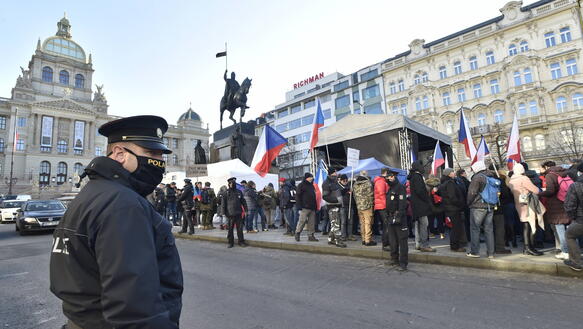 Das Bild zeigt einen öffentlichen Platz, links im Bild eine Polizist, recht mehrere dutzend Menschen mit tschechischen Nationalflaggen