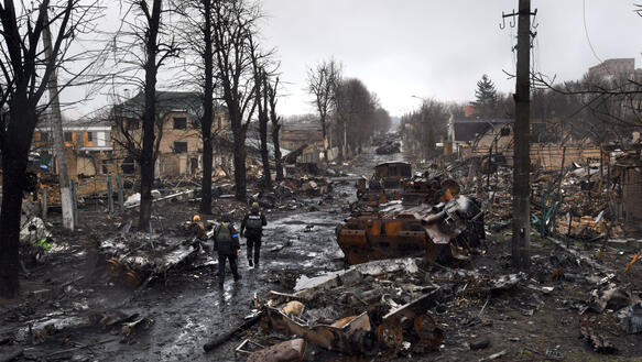 Das Bild zeigt eine Straße mit zerstörten Panzern, Resten von Fahrzeugen und Gebäuden